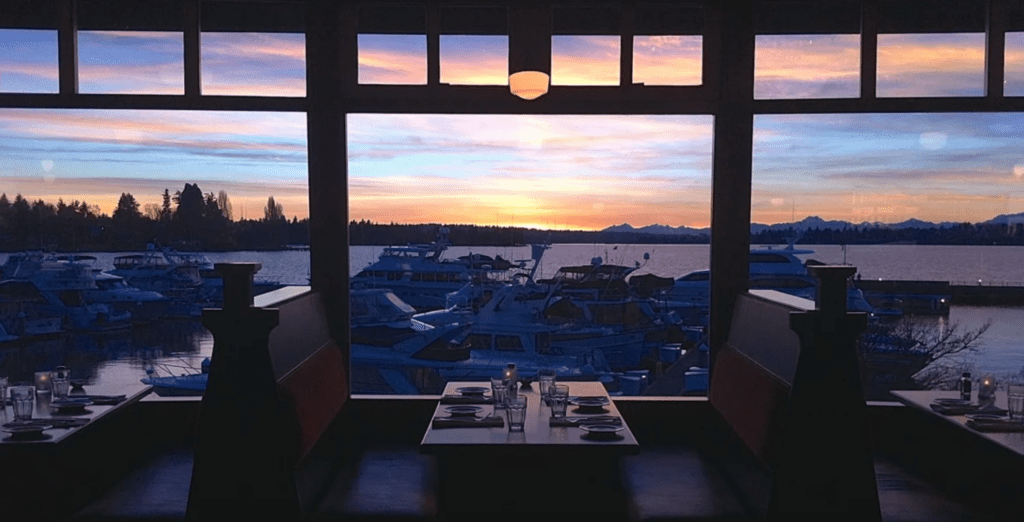 A table with two chairs and a window overlooking the water.