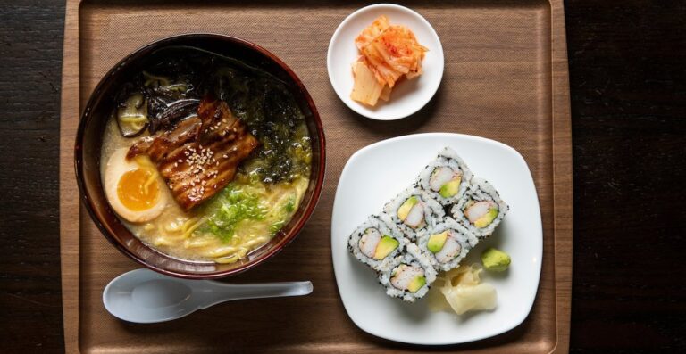 A bowl of soup, sushi and a plate with some vegetables.