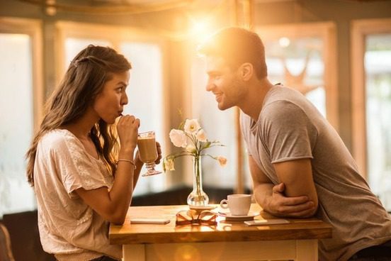 A man and woman sitting at a table with cups.