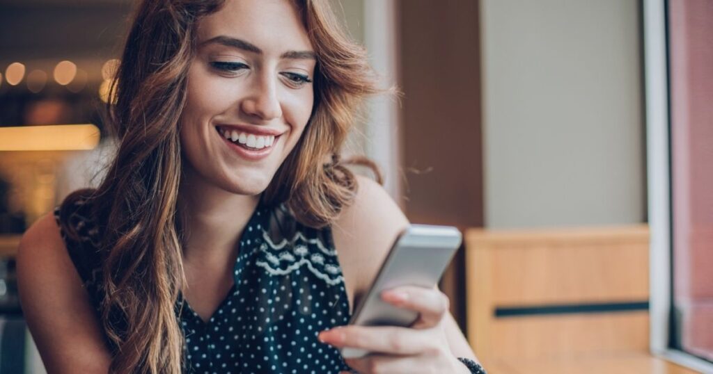 A woman is smiling while looking at her phone.